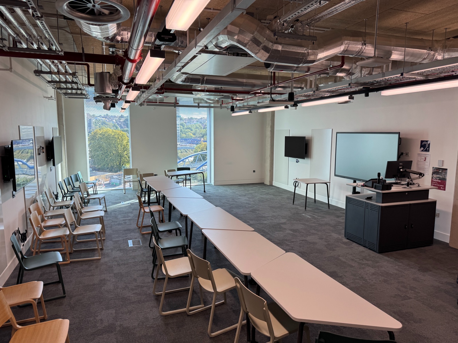 A meeting room with a display screen, tables and chairs, and large windows